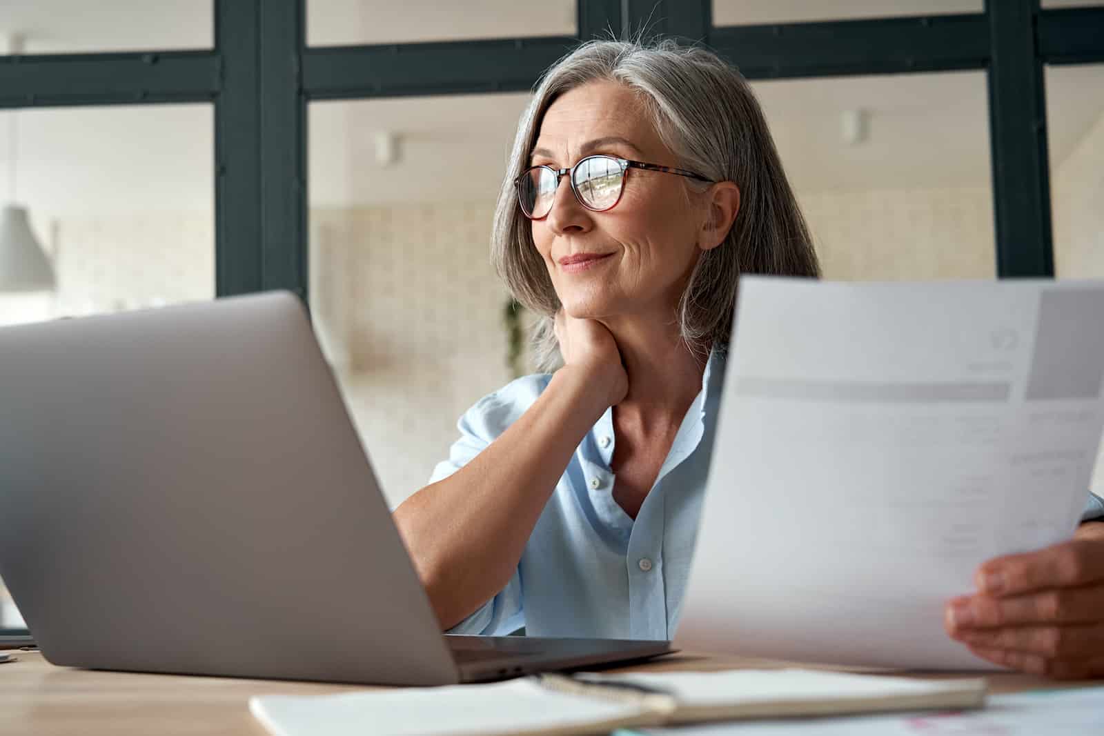 Woman with glasses looking at her computer screen holding a piece of paper
